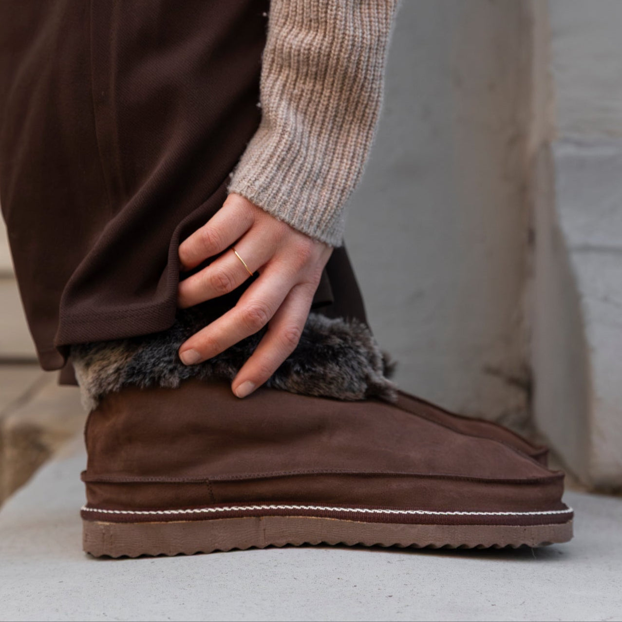 Brown suede boots with fur trim worn by a person, standing on a stone surface.