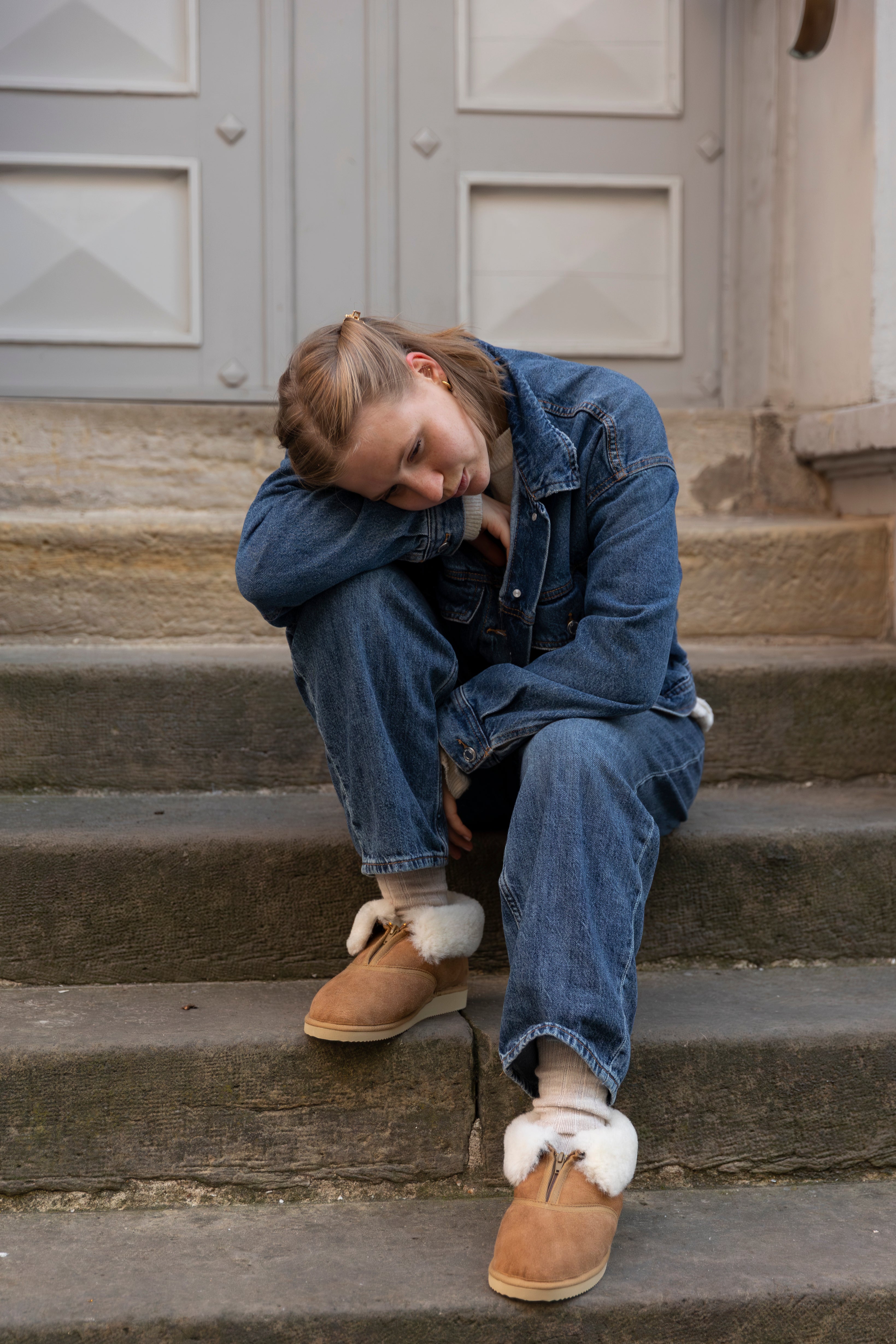 Person sitting on steps wearing denim outfit and UGG slippers.