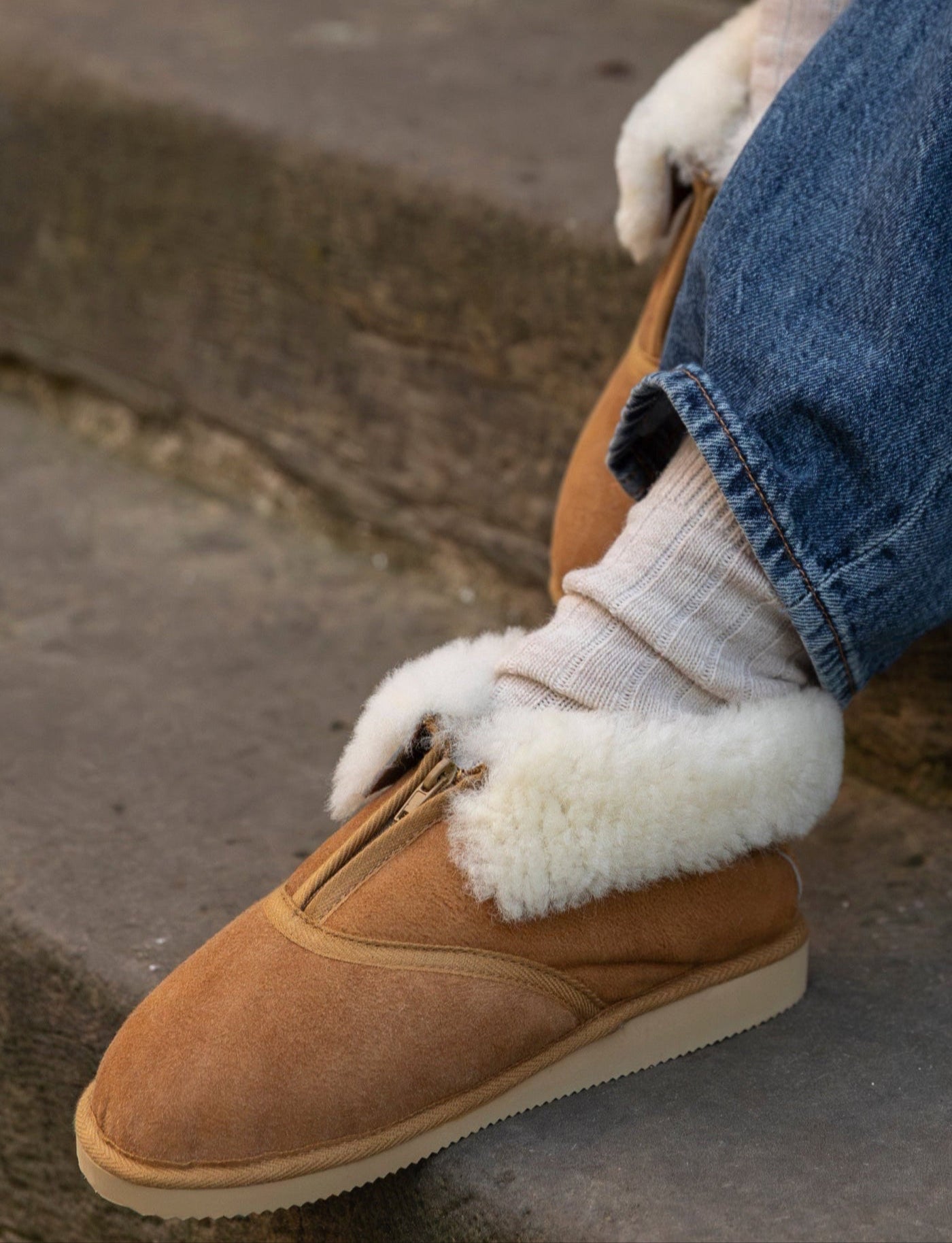 Person wearing brown shoes with white fur trim and blue jeans sitting on steps.